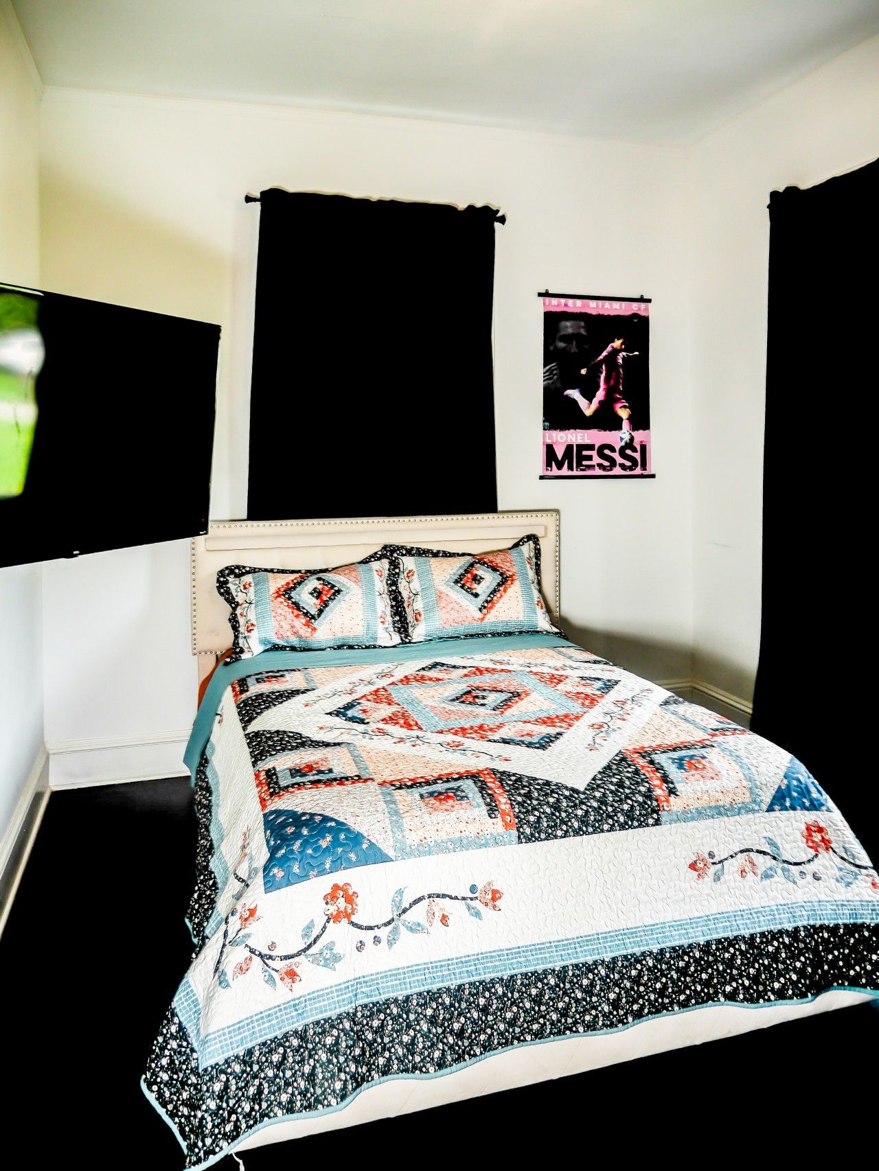 Un lit avec une couette à motifs, des rideaux noirs et une affiche accrochée au mur.