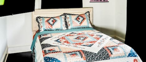 A bed with a patterned quilt, black curtains, and a poster on the wall.