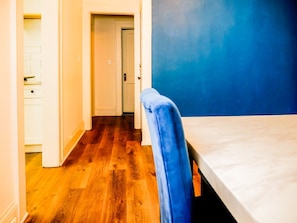 Un passadís estret amb terra de fusta que condueix a una habitació amb una paret blava i un llit.