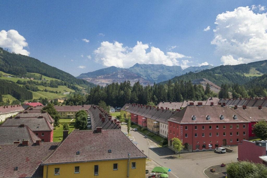 A residential area with red and yellow buildings, a clear sky, and mountains in the background.
