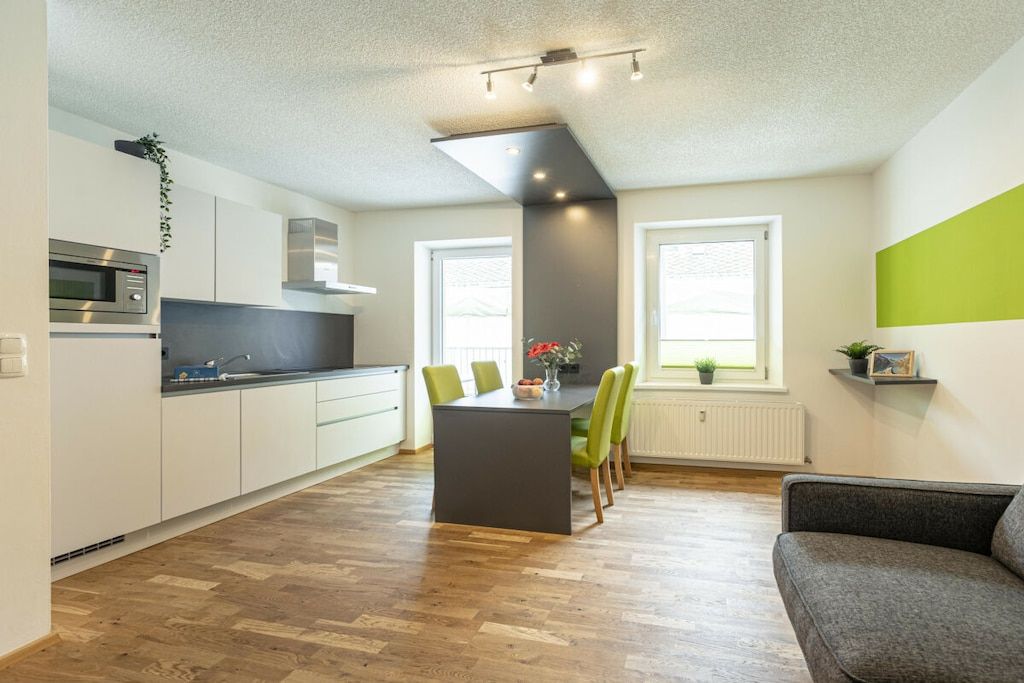 Eine moderne Küche mit Kochinsel, Essstühlen und einer Couch im Wohnbereich mit Blick ins Freie.