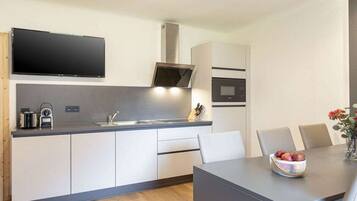 A modern kitchen with a flat-screen TV, built-in oven, and a dining area with a table and chairs.