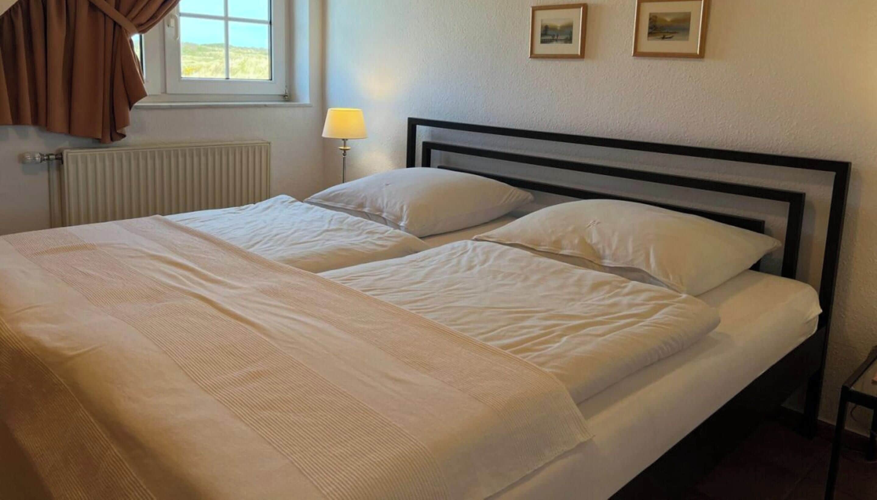 A double bed with white linens, a bedside lamp, and a window with curtains.