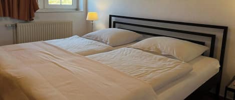 A double bed with white linens, a bedside lamp, and a window with curtains.