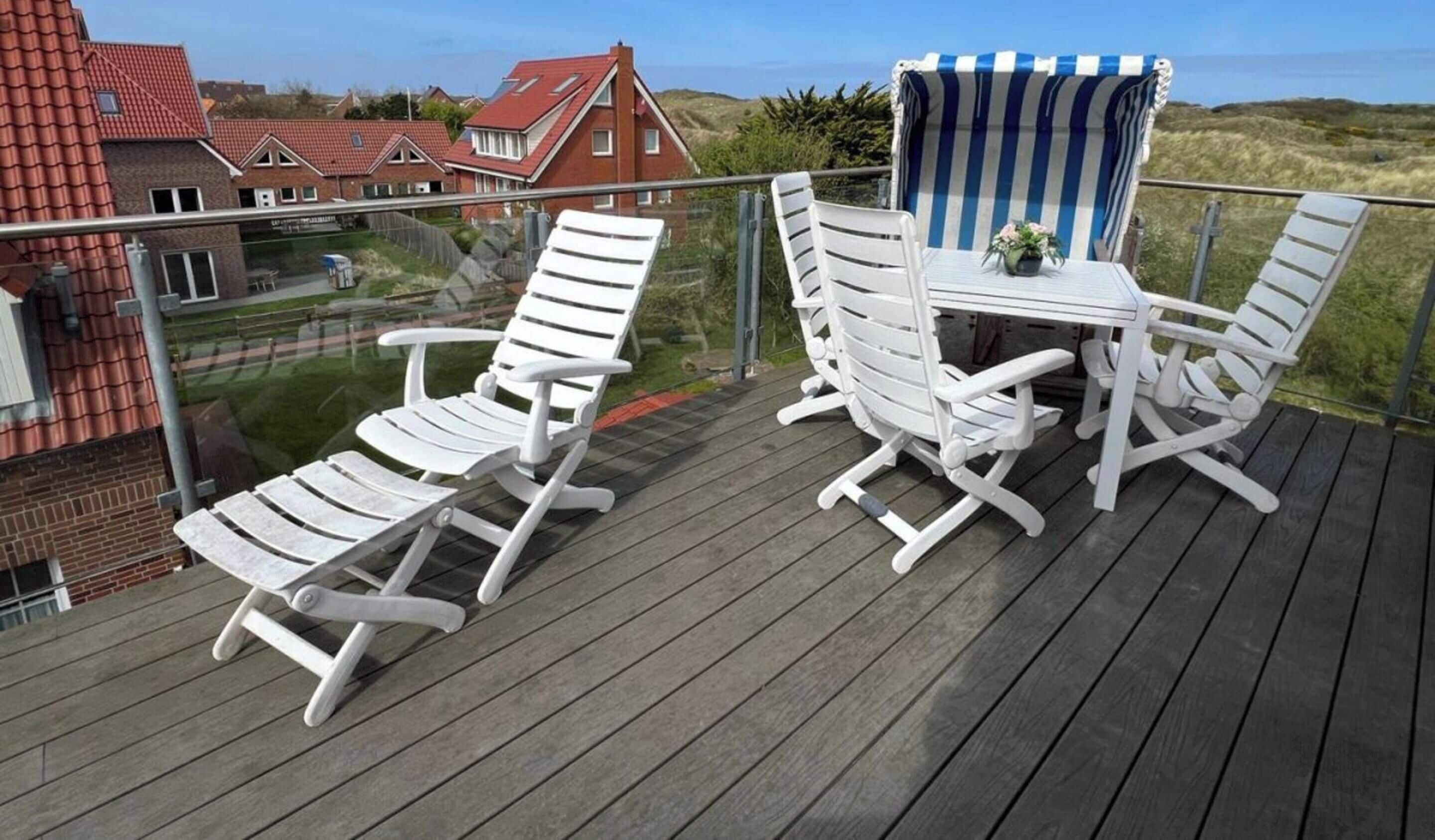 Una terraza con sillas y una mesa blancas, con vista a una zona residencial con casas y al mar.