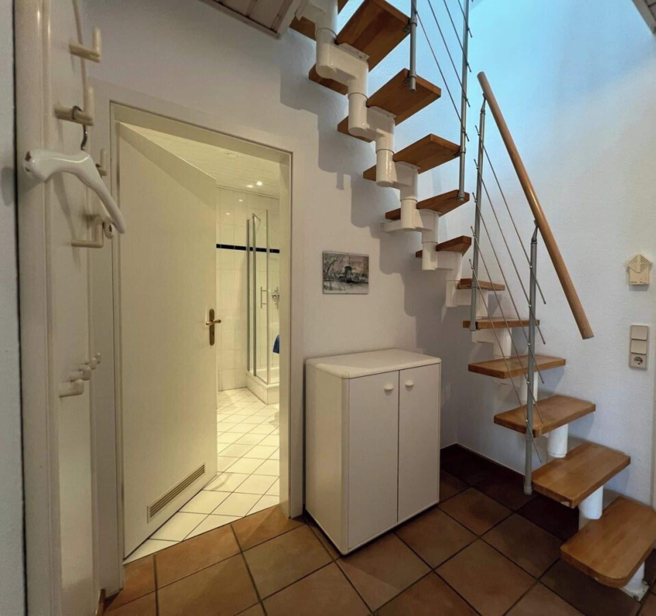 A staircase with wooden steps and white walls, leading to a bathroom with a glass shower enclosure.