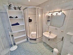 Ein modernes Badezimmer mit einer gläsernen Duschkabine, einem weißen Waschbecken und einem beleuchteten Spiegel.