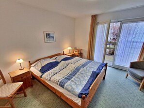 Ein Schlafzimmer mit Bett, Nachttischen, einem Sessel und Blick ins Freie durch eine Schiebetür.