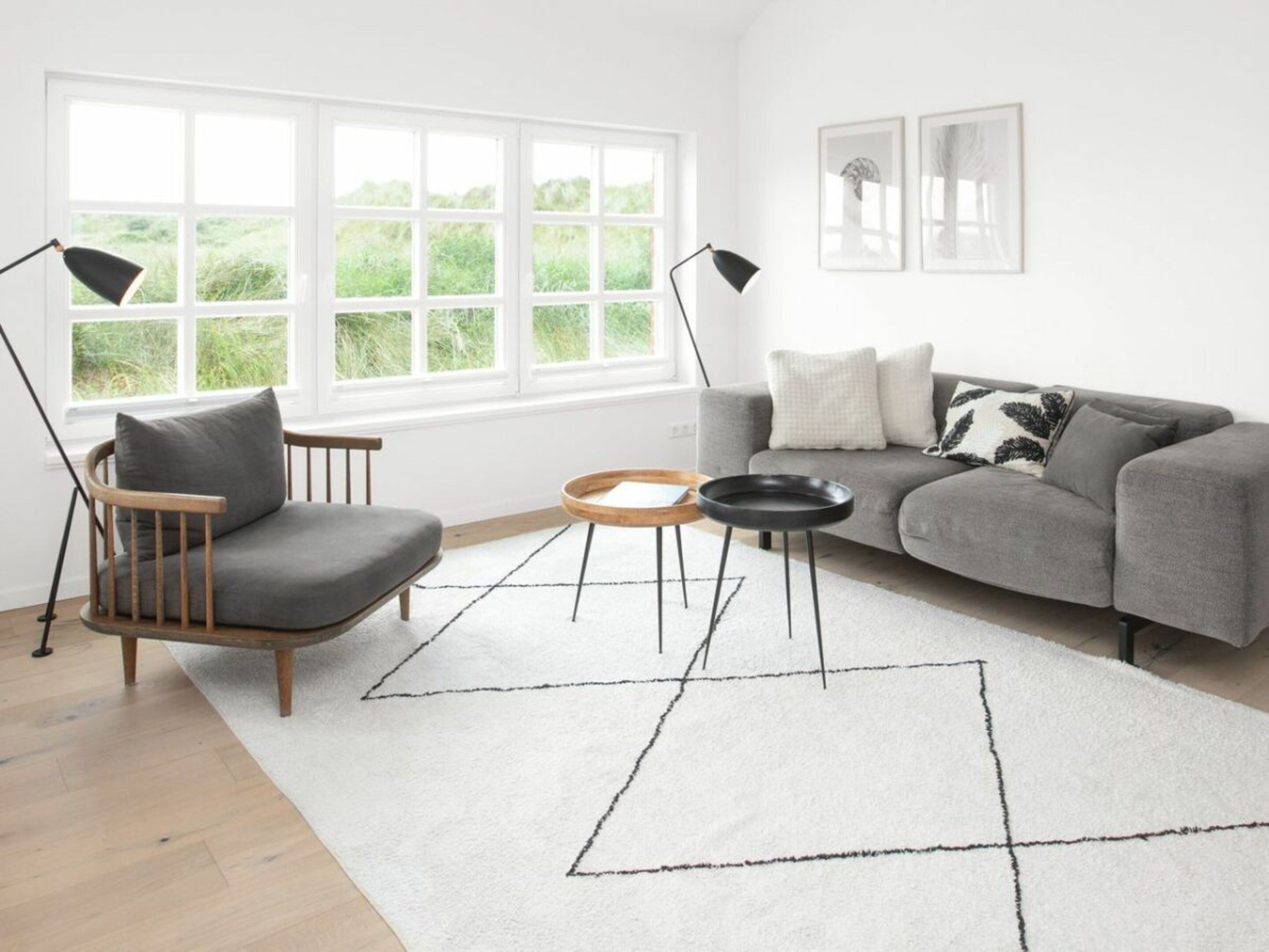 A modern living room with a grey sofa, a wooden chair, a round coffee table, and a white rug with geometric patterns.