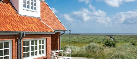 A house with a red-tiled roof, a brick exterior, and a view of a grassy field.