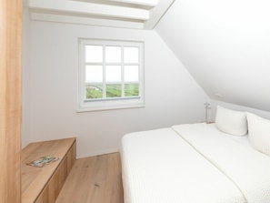 Ein Schlafzimmer mit Dachfenster, einem Fenster mit Blick auf Grünflächen, einer Holzbank und einem Bett mit weißer Bettwäsche.
