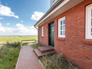 Ein rot backsteinsches Gebäude mit einer grünen Tür, einem Fenster und einem Ziegelweg, der zum Eingang führt.