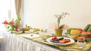 A breakfast buffet with various fruits, vegetables, and a vase of flowers.