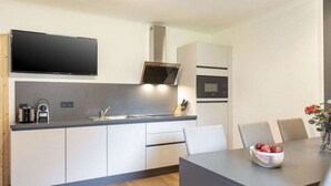 Une cuisine moderne équipée d’un téléviseur à écran plat, d’un four encastré et d’un coin repas avec une table et des chaises.