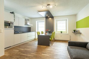 Eine moderne Küche mit Kochinsel, Essstühlen und einer Couch im Wohnbereich mit Blick ins Freie.
