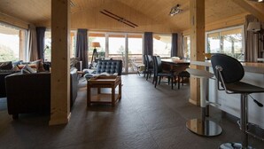 A spacious room with a wooden ceiling, a sofa, a dining table, and a bar area. - Cabin in Turrach with sauna and Wi-Fi (Turrach)