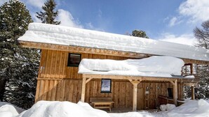 Een houten blokhut met een overdekte veranda en een bank, omgeven door sneeuw.