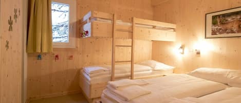A wooden cabin room with bunk beds, a window with a view, and a wall-mounted light fixture.