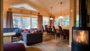 Een gezellig interieur van een chalet met een bank, eettafel, stoelen en een houtkachel.