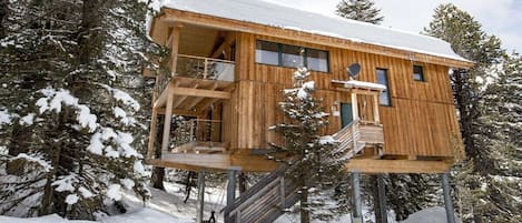 A wooden cabin with a balcony, surrounded by snow-covered trees.