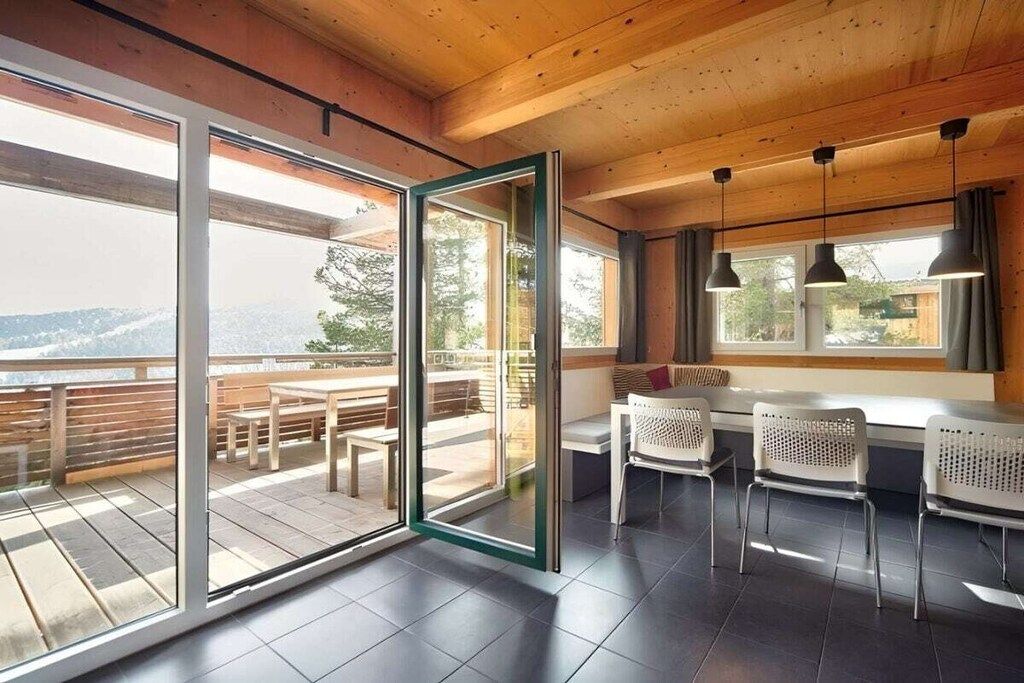 A modern interior with a wooden ceiling, large sliding glass doors leading to an outdoor deck, and a seating area with white chairs.