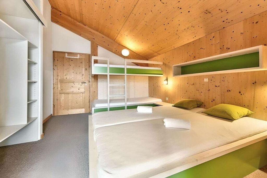 Quarto com beliches, uma escada e uma parede verde.