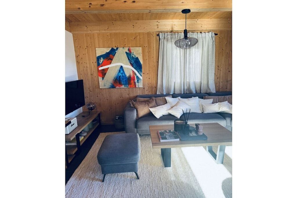 Ein modernes Wohnzimmer mit einer Couch, Hocker, Couchtisch und Kunstwerken an der Wand.