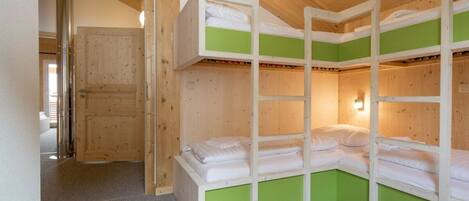 Une pièce avec des lits superposés, une porte en bois et un luminaire.
