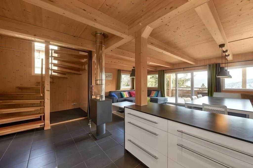 A modern kitchen with wooden beams, a central island, and a dining area with a view.