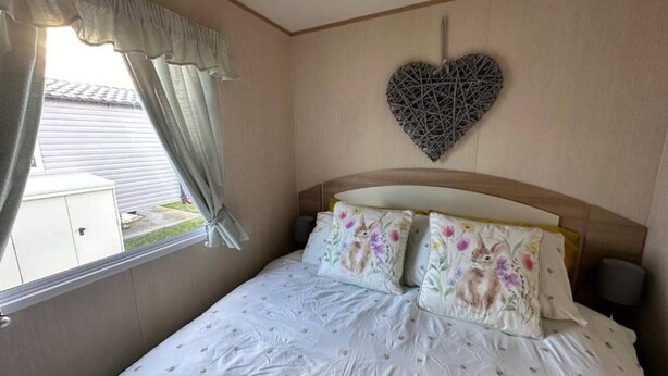 A bedroom with a bed, curtains, a heart-shaped wall decoration, and a window.