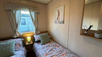 Quarto com duas camas de solteiro, janela com cortinas, um quadro na parede e mesa de cabeceira com abajur.