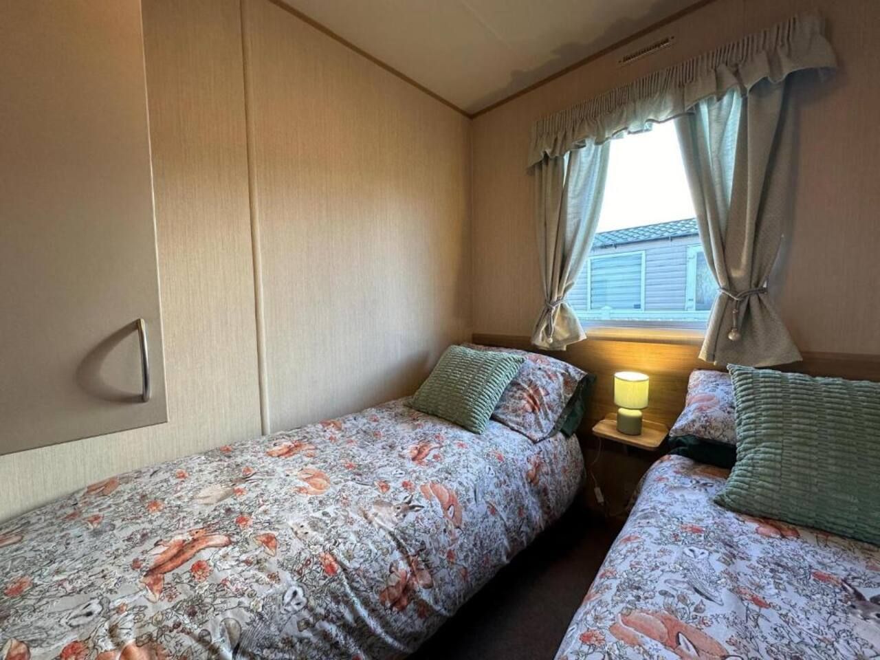 Ein Schlafzimmer mit zwei Einzelbetten, einem Nachttisch mit Lampe und einem Fenster mit Vorhängen.