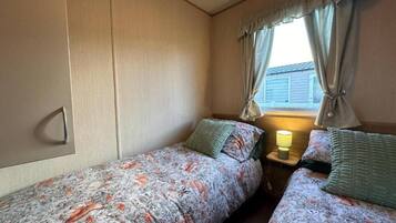 Ein Schlafzimmer mit zwei Einzelbetten, einem Nachttisch mit Lampe und einem Fenster mit Vorhängen.