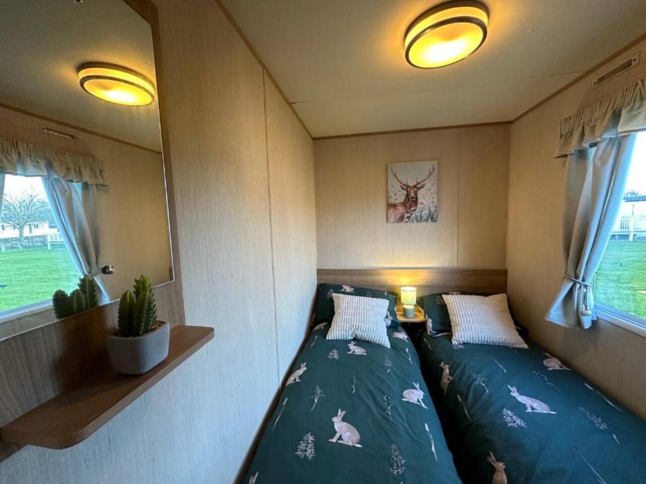 A bedroom with two beds, a nightstand with a lamp, a wall-mounted painting, and a window with curtains.