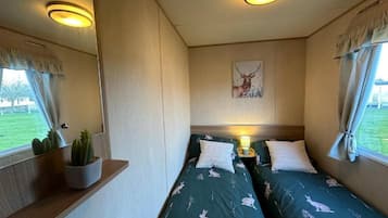 A bedroom with two beds, a nightstand with a lamp, a wall-mounted painting, and a window with curtains.