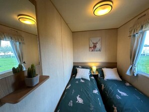 A bedroom with two beds, a nightstand with a lamp, a wall-mounted painting, and a window with curtains.