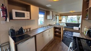 A compact kitchen with a microwave, kettle, and stove, a small refrigerator, and a window with a view of the outside.
