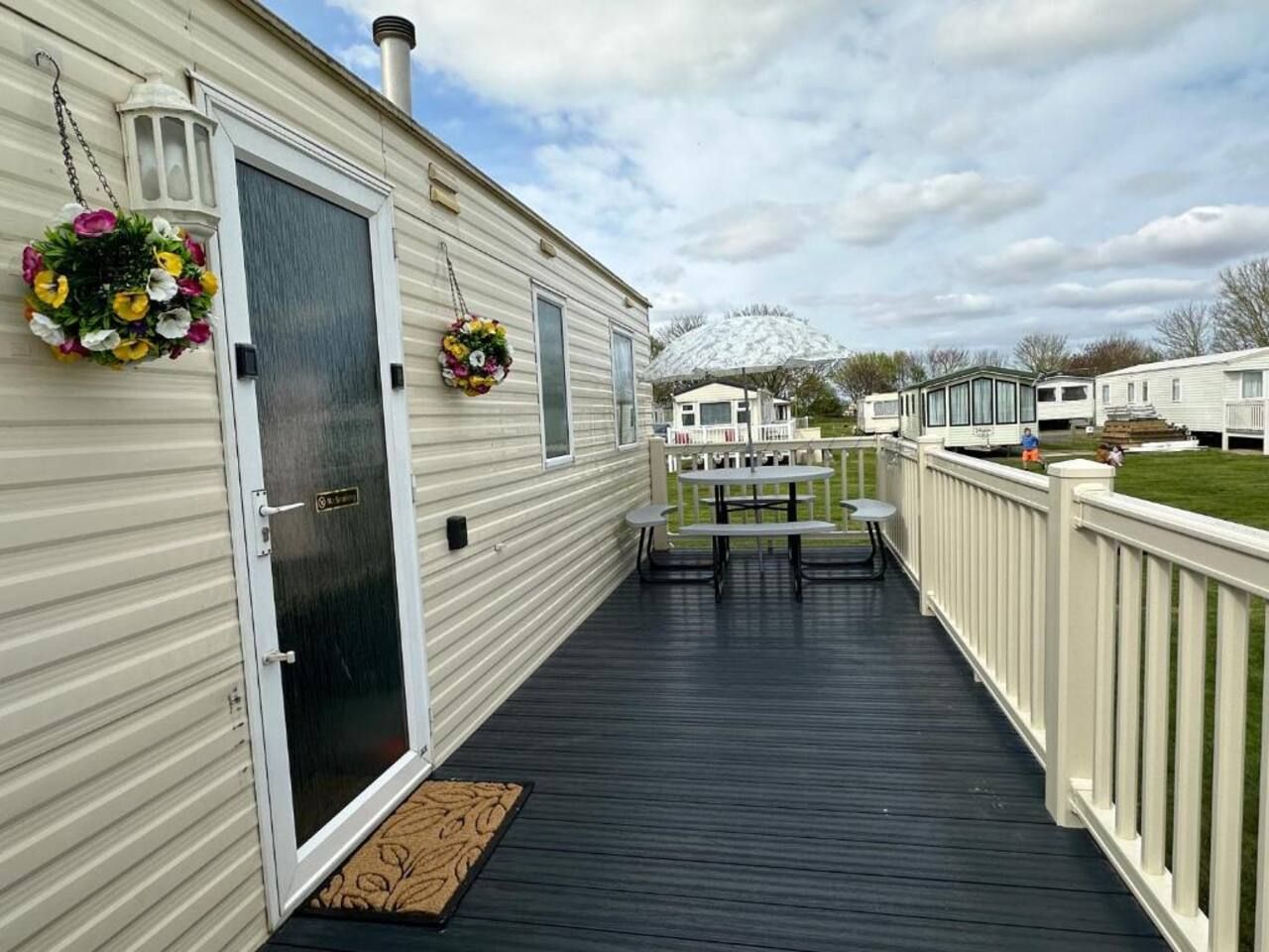A covered deck with a table and chairs, a door, and hanging flower baskets.