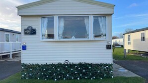 A mobile home with a flat roof, a front window with curtains, and a small porch.