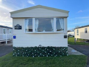 A mobile home with a flat roof, a front window with curtains, and a small porch.