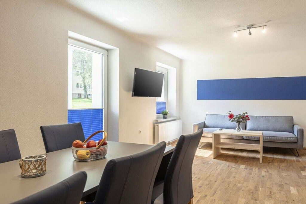 Ein modernes Wohnzimmer mit Essbereich, einem an der Wand befestigten Flachbildfernseher und einem Sofa mit kleinem Tisch.