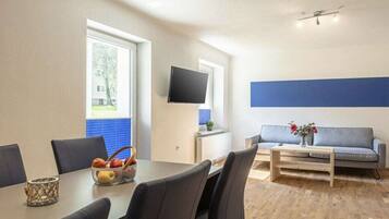 Ein modernes Wohnzimmer mit Essbereich, einem an der Wand befestigten Flachbildfernseher und einem Sofa mit kleinem Tisch.
