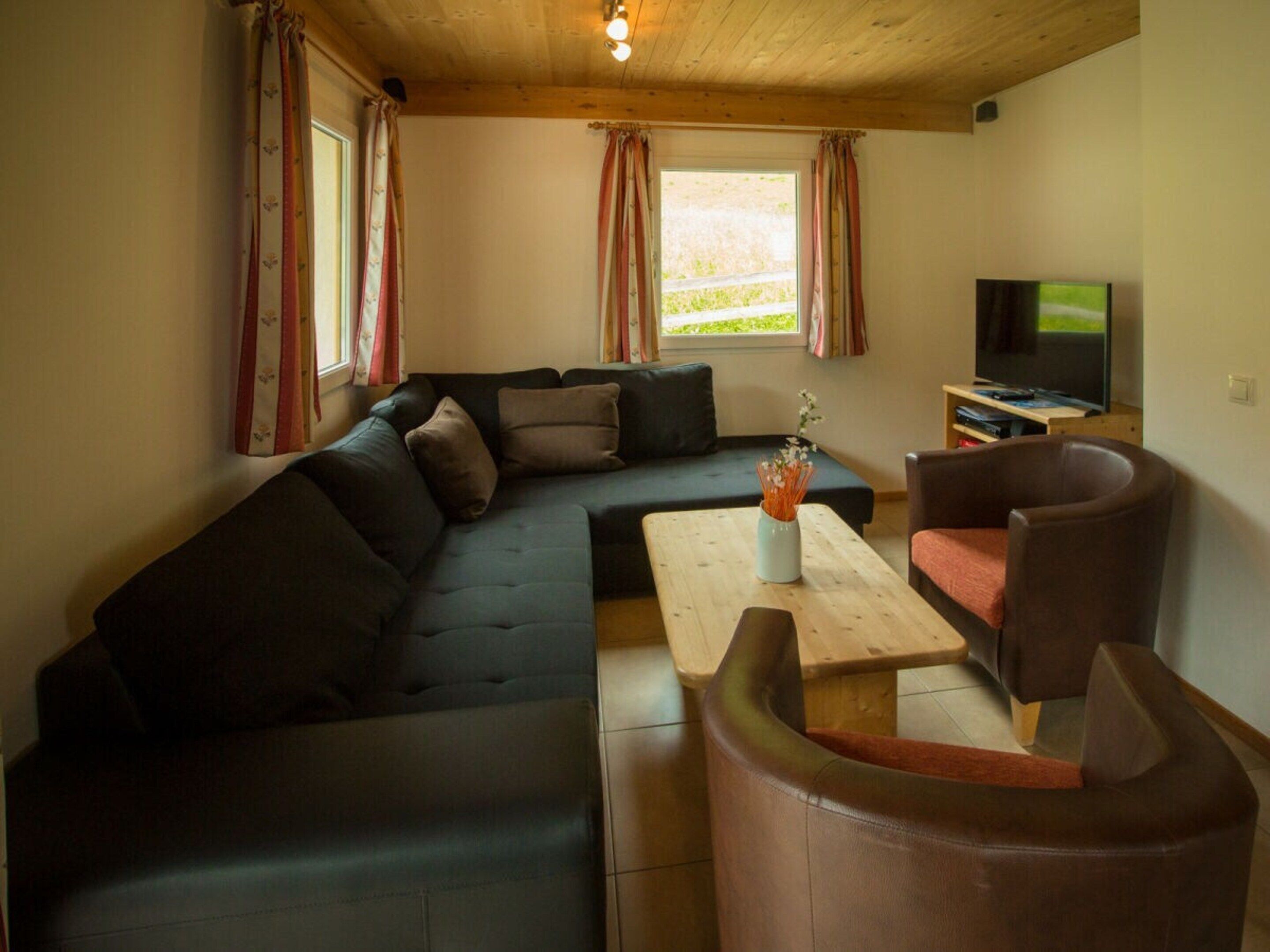A cozy living room with a sectional sofa, a coffee table, a TV, and a window with curtains.