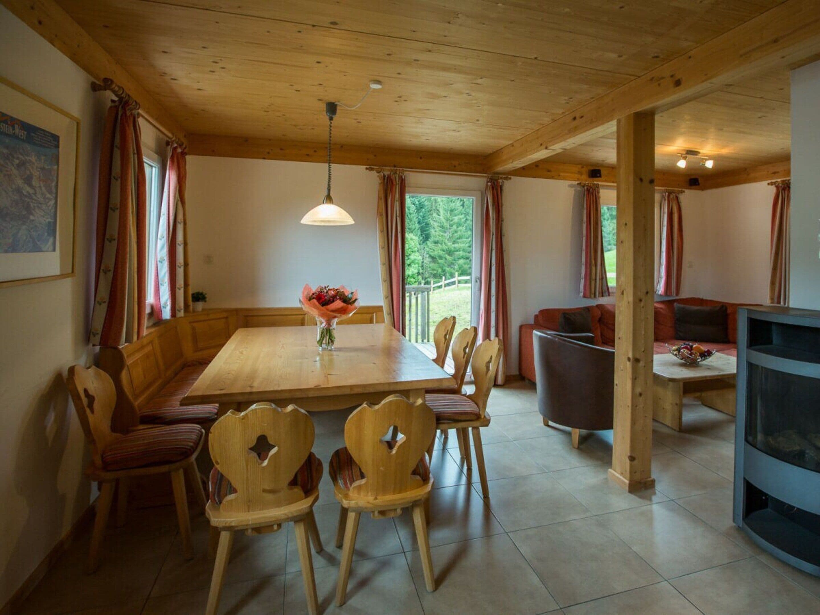 A wooden dining area with a table and chairs, a vase of flowers, and a television on a stand.