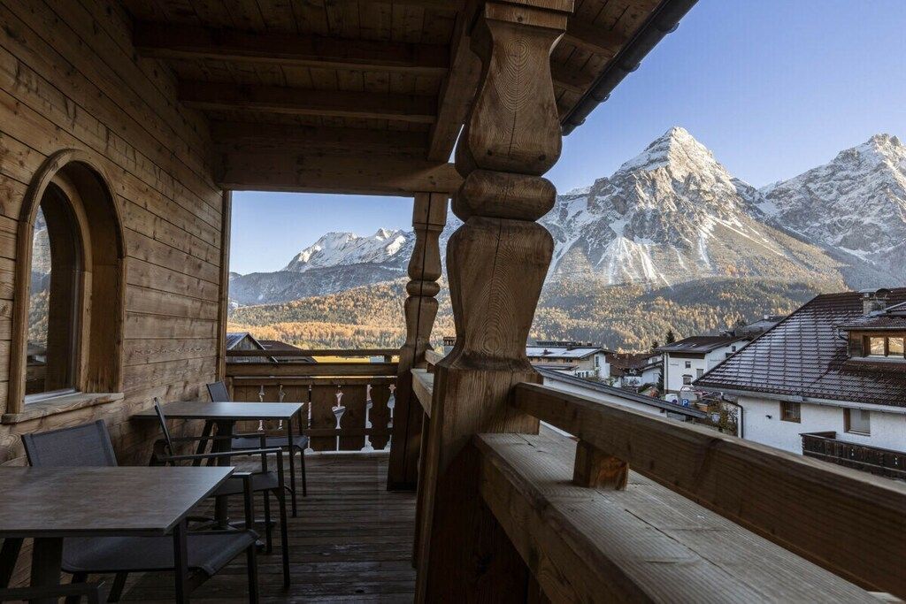 A wooden balcony with tables and chairs, overlooking a mountain range.