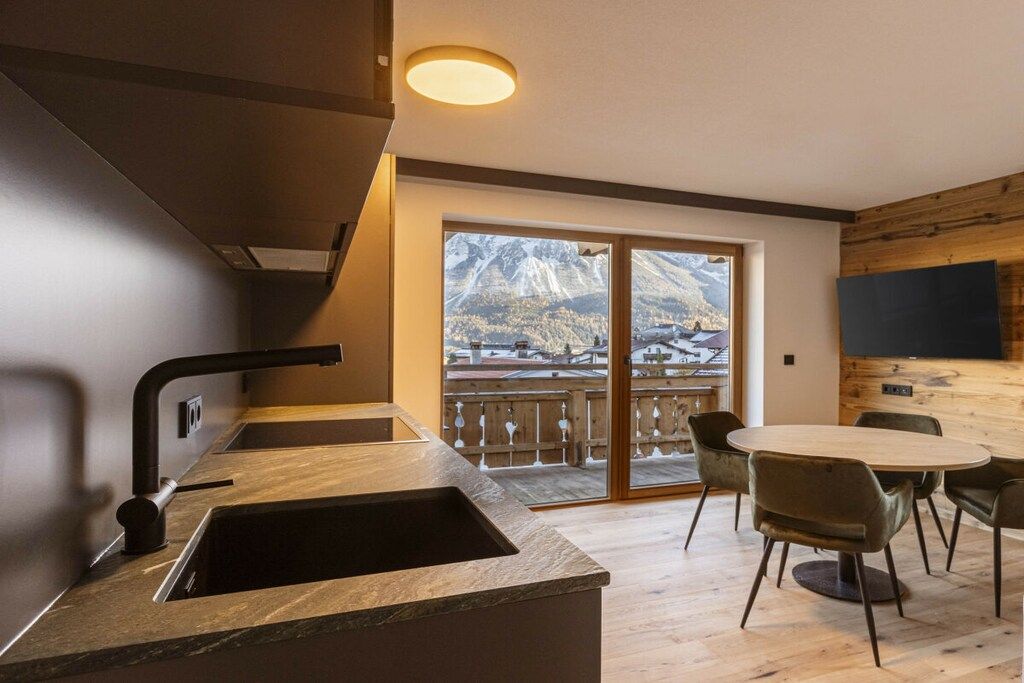 A modern kitchen with a built-in sink, a dining area with a round table and chairs, and a large window offering a mountain view.
