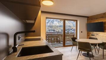 A modern kitchen with a built-in sink, a dining area with a round table and chairs, and a large window offering a mountain view.