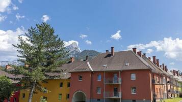 A row of multi-story buildings with balconies, a clear sky, and a mountain in the background.