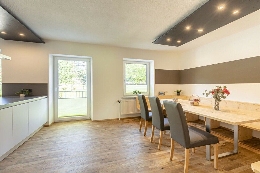 Une cuisine moderne avec une table et des chaises en bois, de grandes fenêtres et une vue sur la verdure.