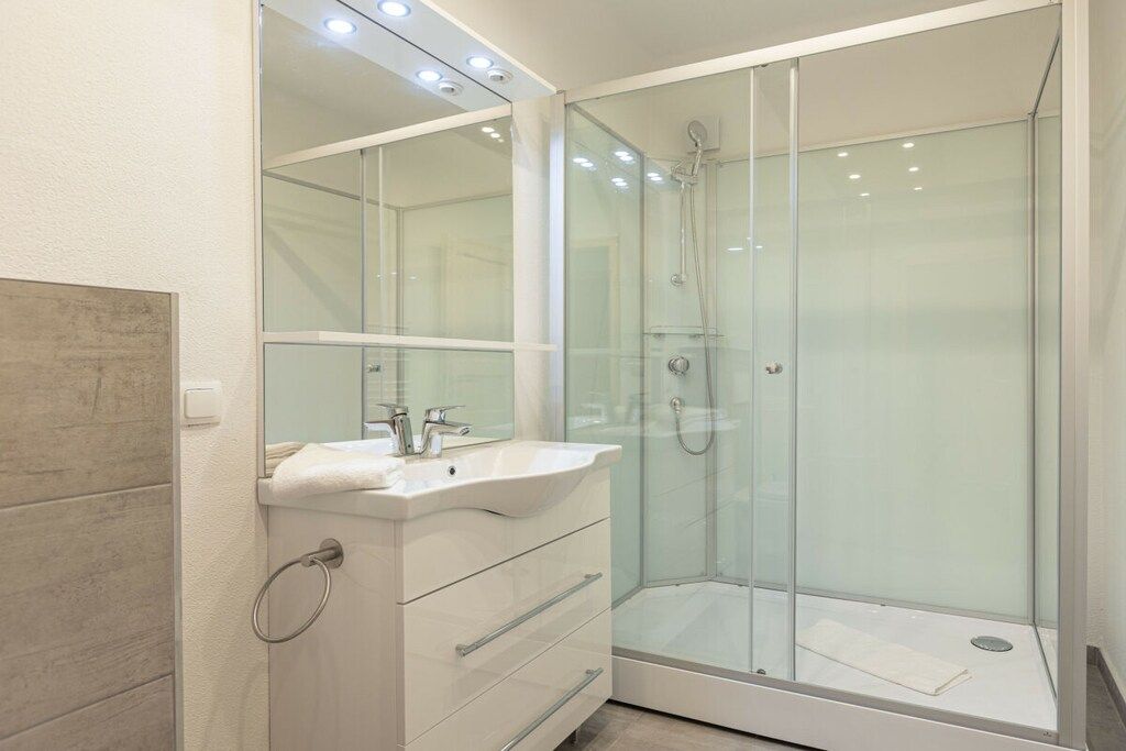 A modern bathroom with a glass-enclosed shower, a white vanity with a mirror, and a tiled floor.